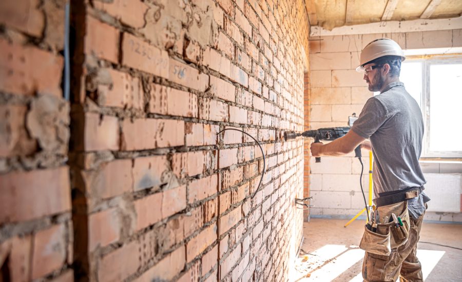 Handyman at a construction site in the process of drilling a wall with a perforator.